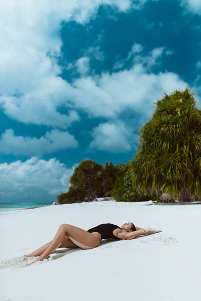 During the day wearing black bikini woman lying on the white sand beach
